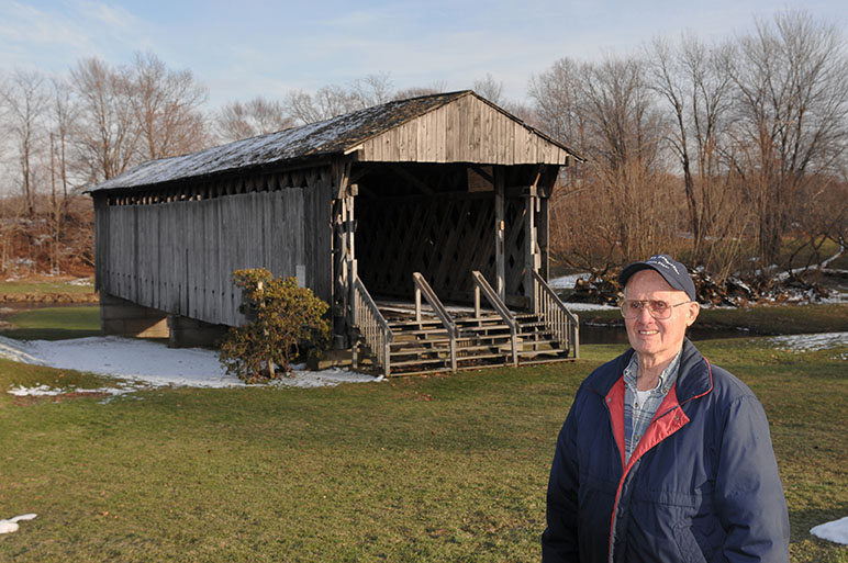 Bob Benson stands in front of the Graham Road bridge in Pierpont Township. He and his late wife donated the land that the bridge was moved to in 1971, after the old bridge was replaced. His grandfather helped build the bridge. Photo by Carl E. Feather/Feather Cottage Media.