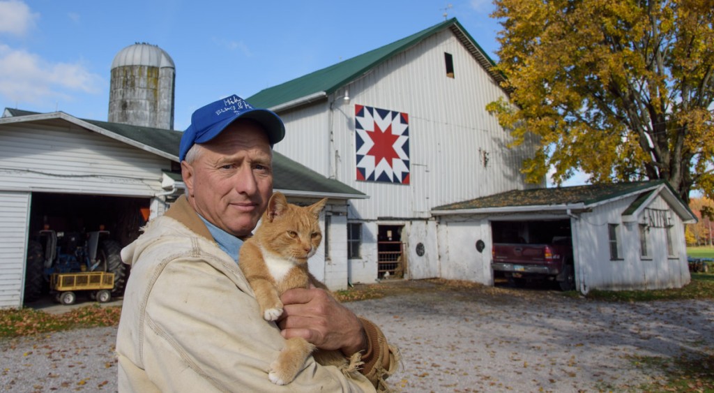 Ted Ewing stands with one of the farm cats in front of the barn that his father, George, built in 1962.