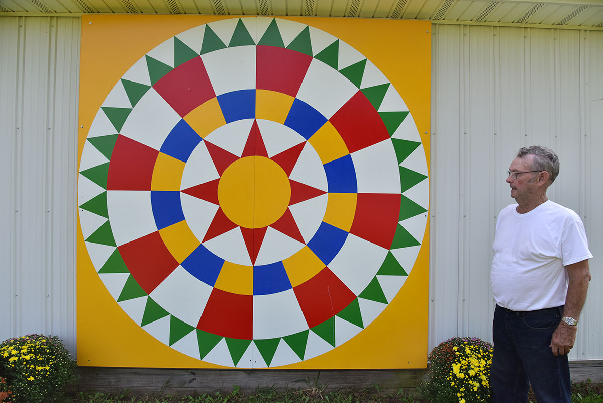 Gary Tabor stands next to the barn quilt he painted and installed on his toy museum in Williamsfield Township