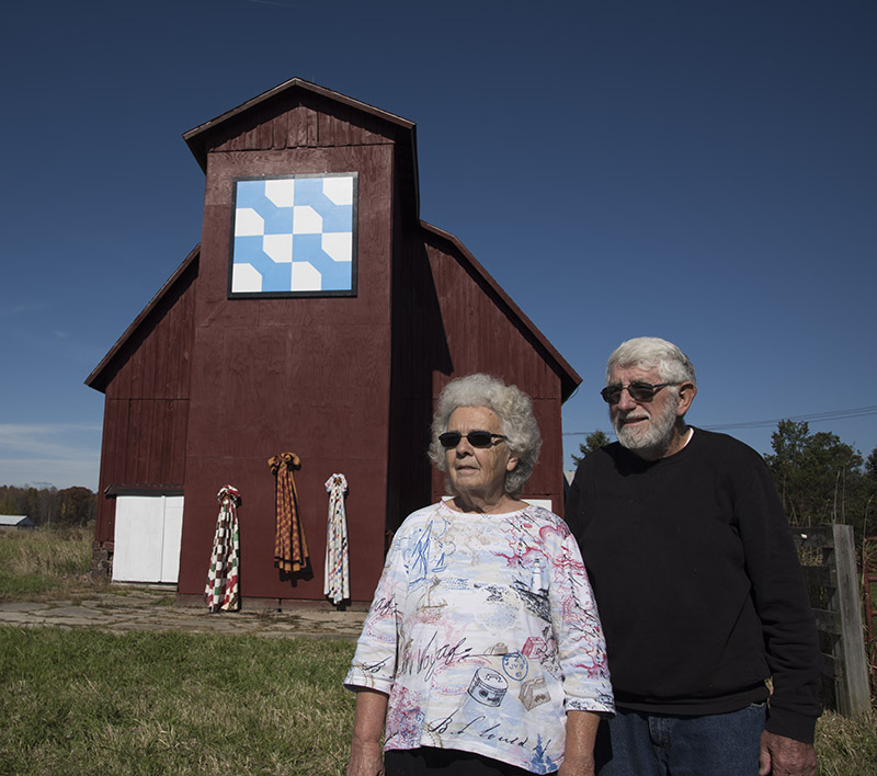 Evelyn Zaebst (left) and Melvin Marrison stand in front of their 1920 barn. Three of Evelyn's bow tie quilts hang below the barn quilt.
