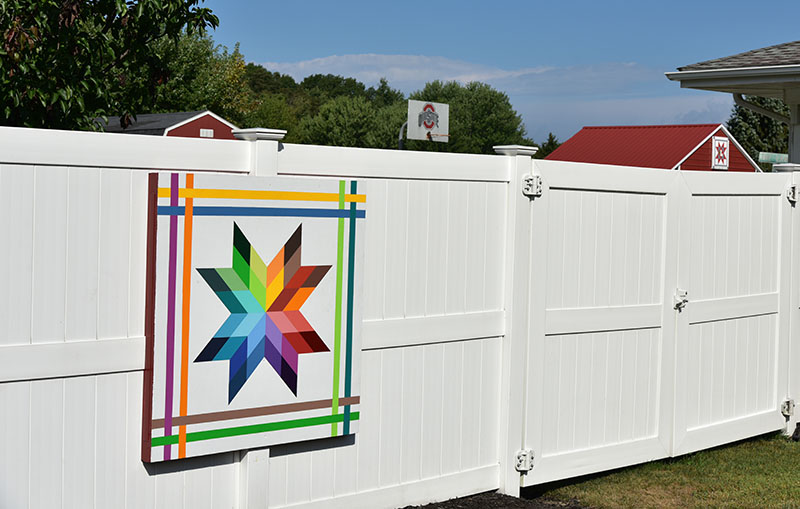 The Rainbow Star quilt on the fence is one of two BQ's at this address. The second (in background) is on the garage and may not be visible if the fence opening is closed. Both are 4-by-4 feet.